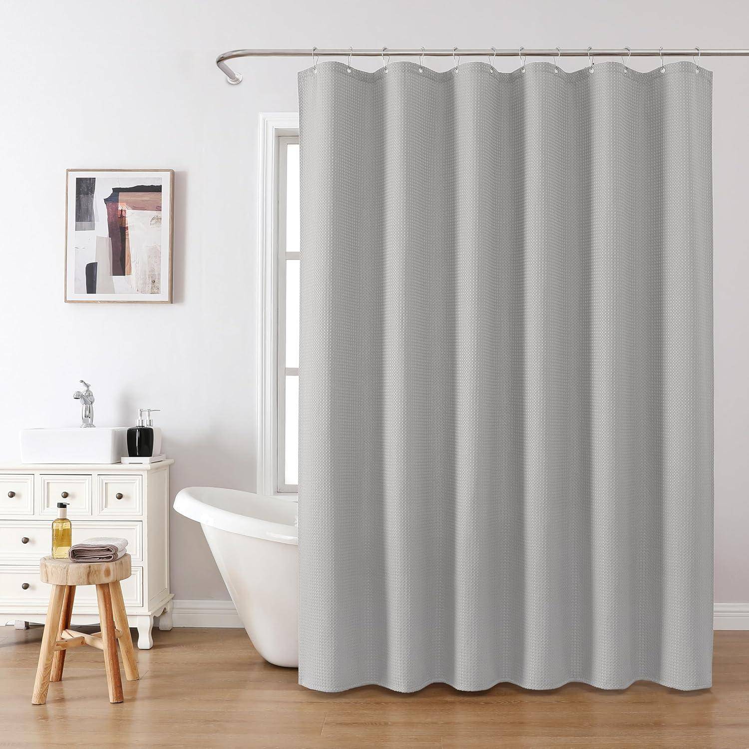 Ein Badezimmer mit einem grauen Duschvorhang, einer weißen Badewanne, einem Waschbecken mit Toilettenartikel, helzem Holzboden und Wandkunst.