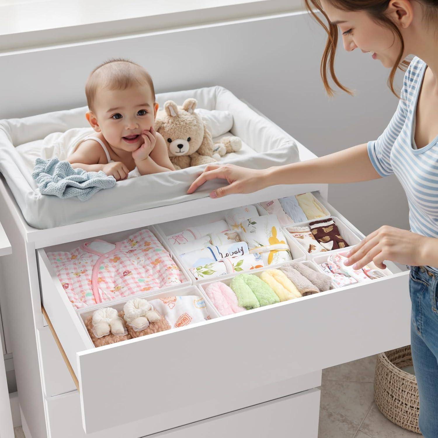 Ein Baby liegt auf einem Wickeltisch und lächelt zu einer Frau, die Babykleidung in einer Schublade nebenan sortiert. Ein Plüschtier liegt neben dem Baby.