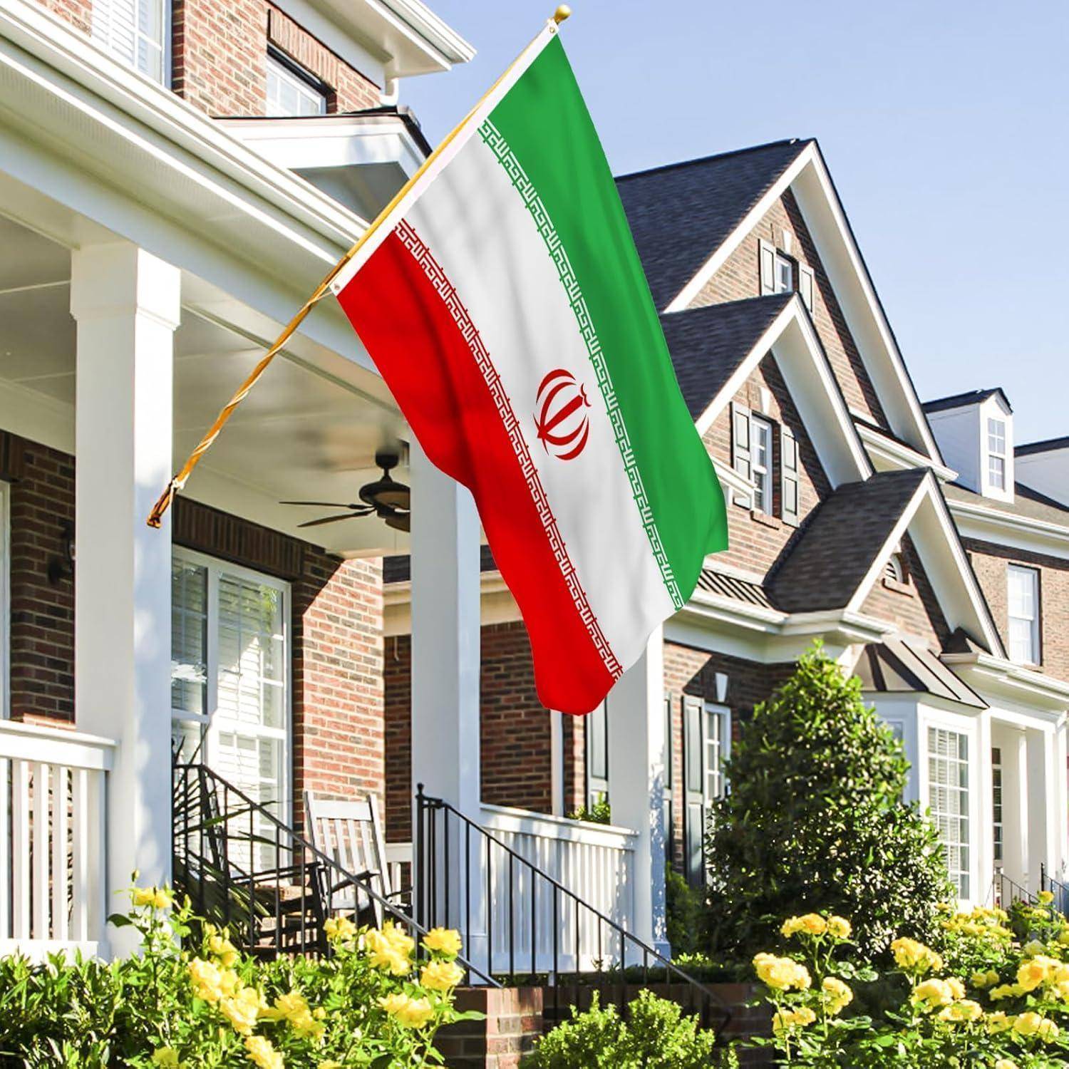 Eine iranische Flagge weht auf der Veranda eines Vorstadthauses, umgeben von Grünanlage an einem sonnigen Tag.