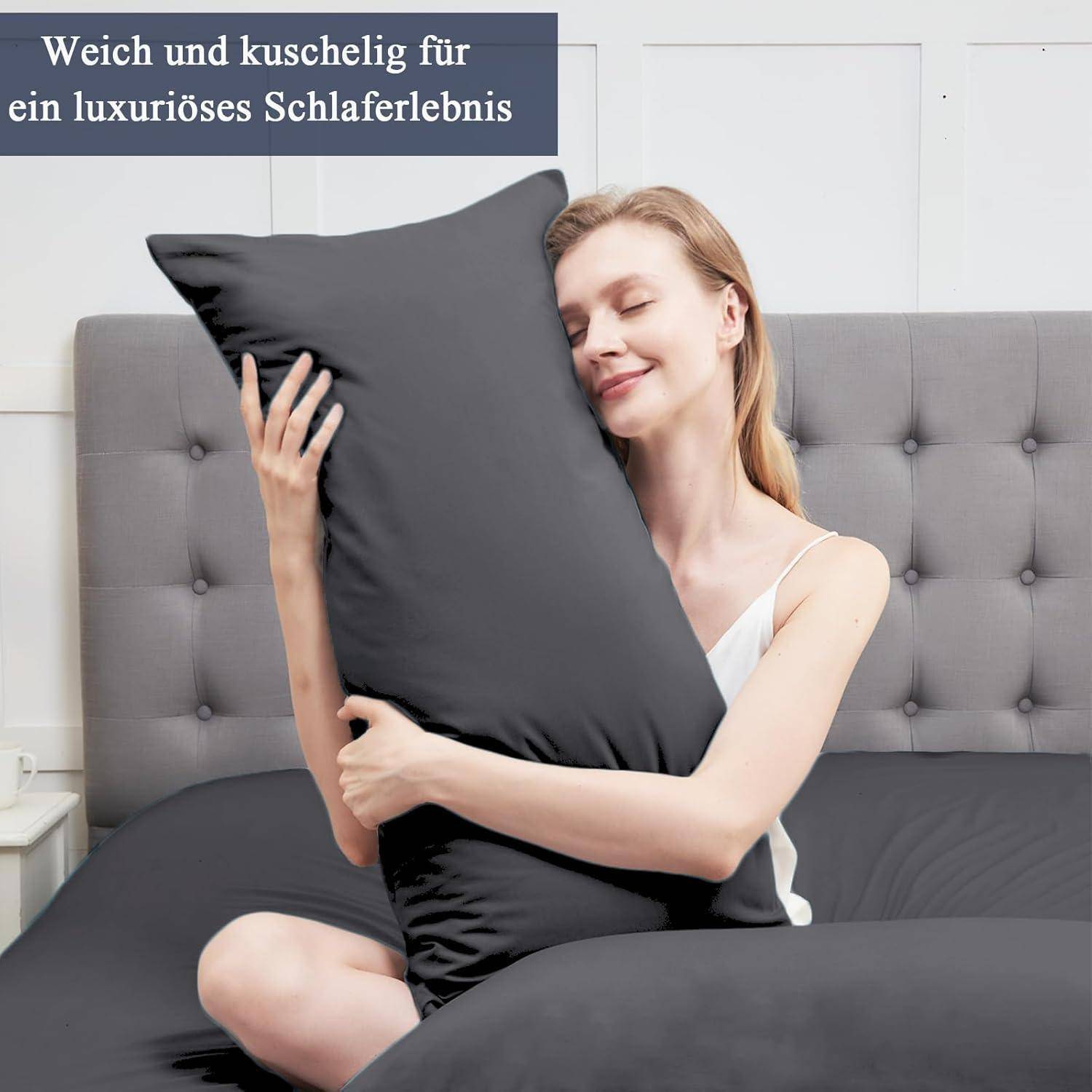 Eine Frau in Weiß umarmt ein schwarzes Kissen auf einem grauen Bett und lächelt mit geschlossenen Augen. Der deutsche Text im Bild betont Luxus und Weichheit.