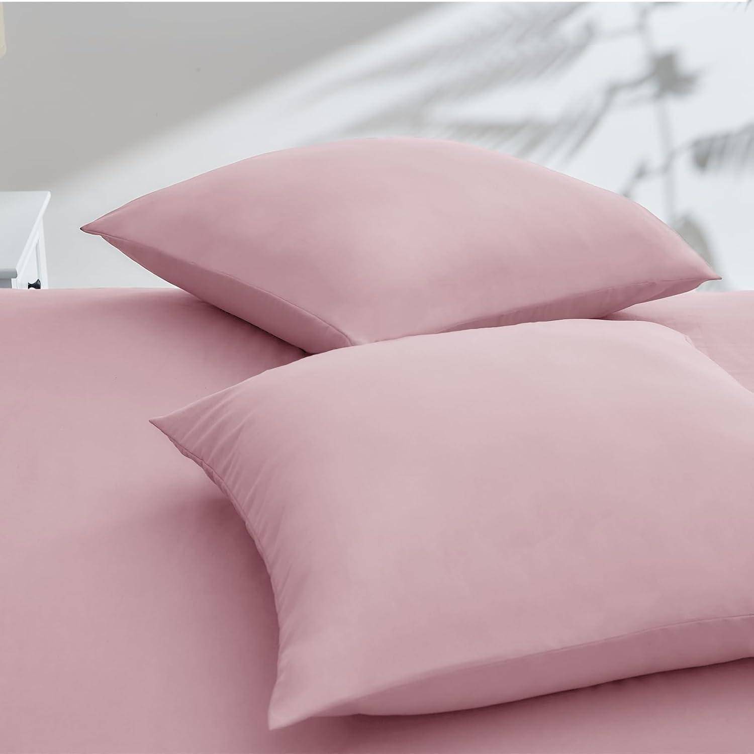 Zwei rosa Kissen auf einer passenden Tagesdecke, die in einer minimalistischen Schlafzimmerumgebung einen weichen, aufeinander abgestimmten Look schaffen.