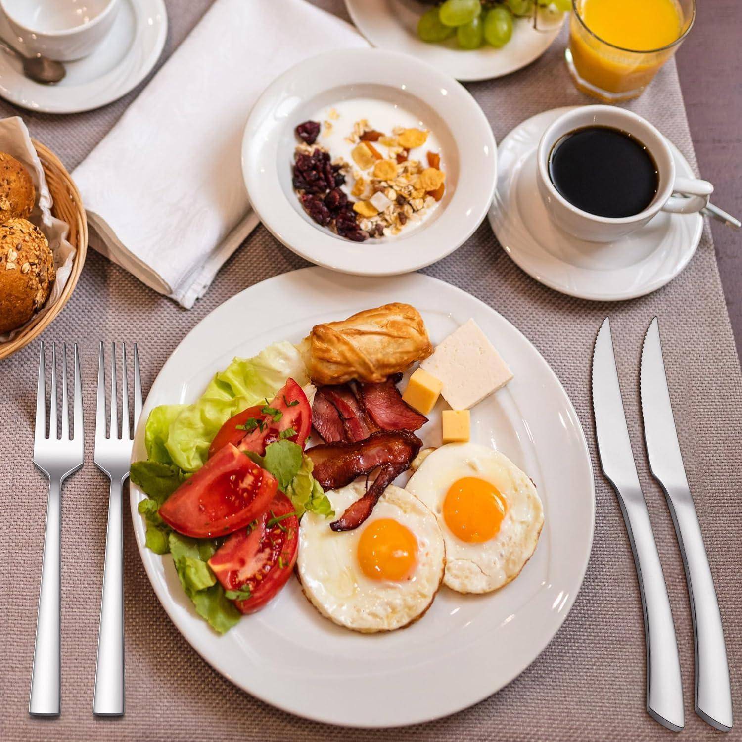 Ein Frühstücksarrangement mit einem Teller, der gebratene Eier, Speck, Tomaten, Salat, Käse und ein Croissant zeigt, dazu eine Tasse Kaffee und ein Glas Saft.