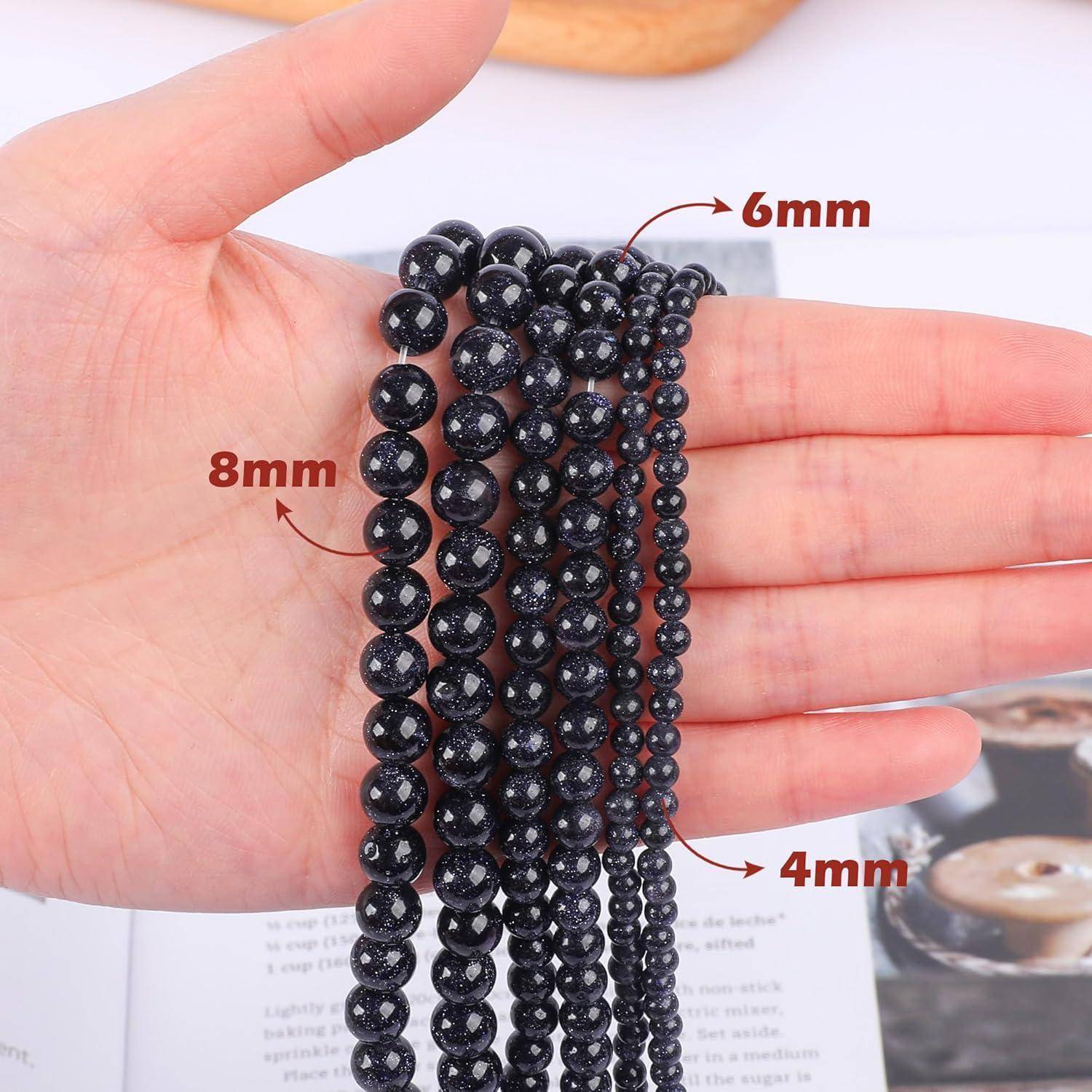 Eine Hand hält Stränge dunkelblauer Perlen in verschiedenen Größen: 8 mm, 6 mm und 4 mm, die die unterschiedlichen Durchmesser veranschaulichen.