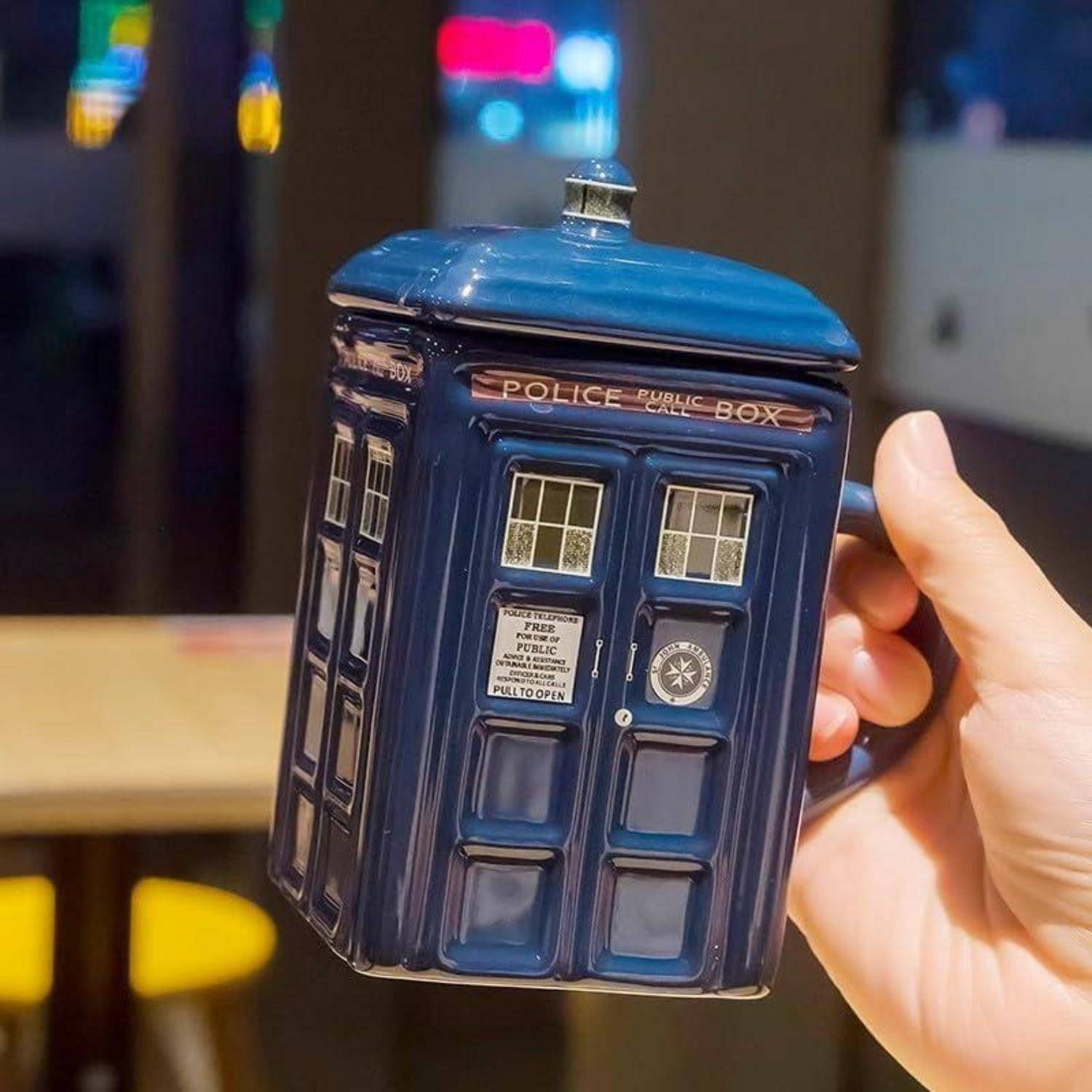 Eine Hand hält eine Keramik-Teekanne in Form einer klassischen britischen Polizeizelle mit blauer Außenseite und den Worten 'POLICE PUBLIC CALL BOX'.