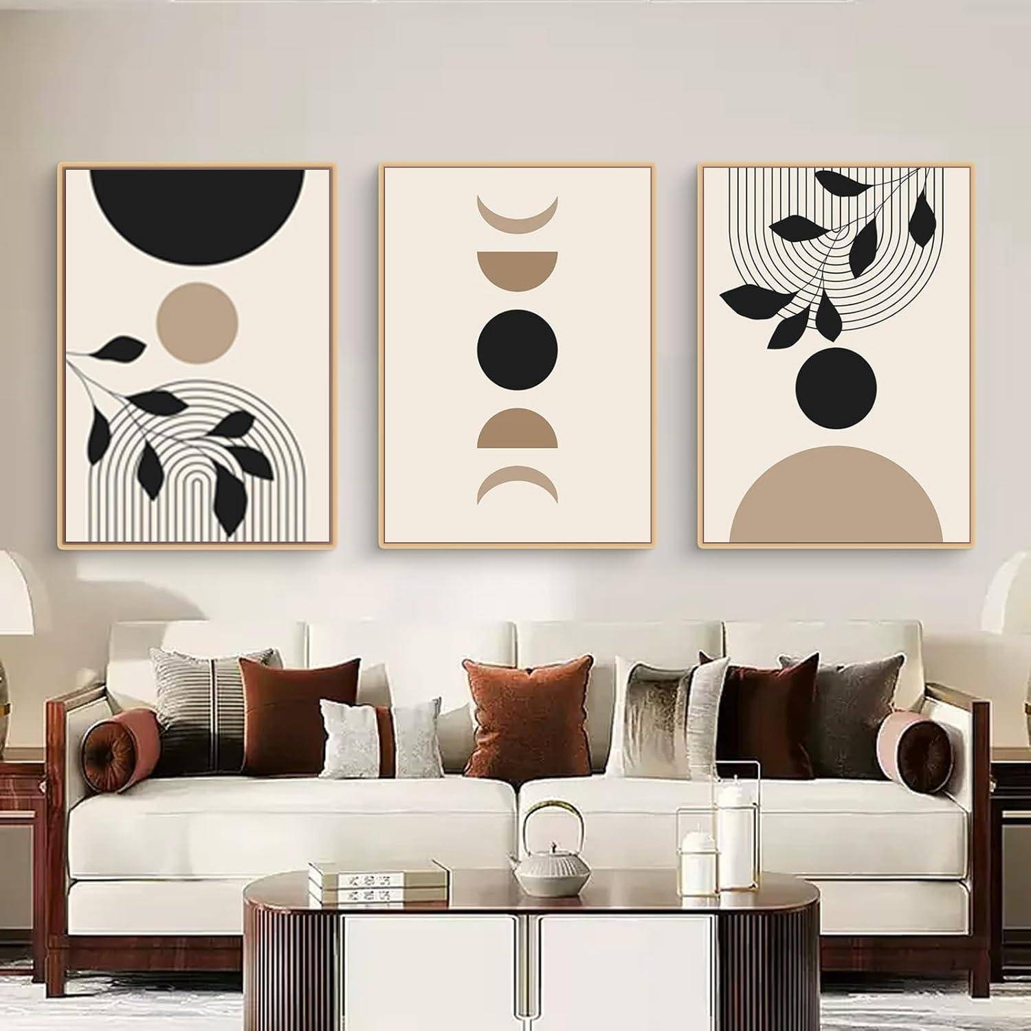 Drei abstrakte Kunstdrucke hängen über einem modernen Sofa. Die Drucke zeigen geometrische Formen und Blattmotive in Schwarz, Beige und Braun.
