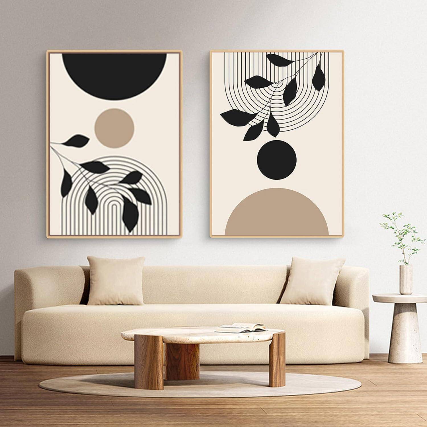 Ein beiger Couch mit weißen Kissen steht mittig unter zwei abstrakten gerahmten Kunstwerken. Auf einem Holztisch liegen Bücher, und rechts daneben steht eine Pflanze.