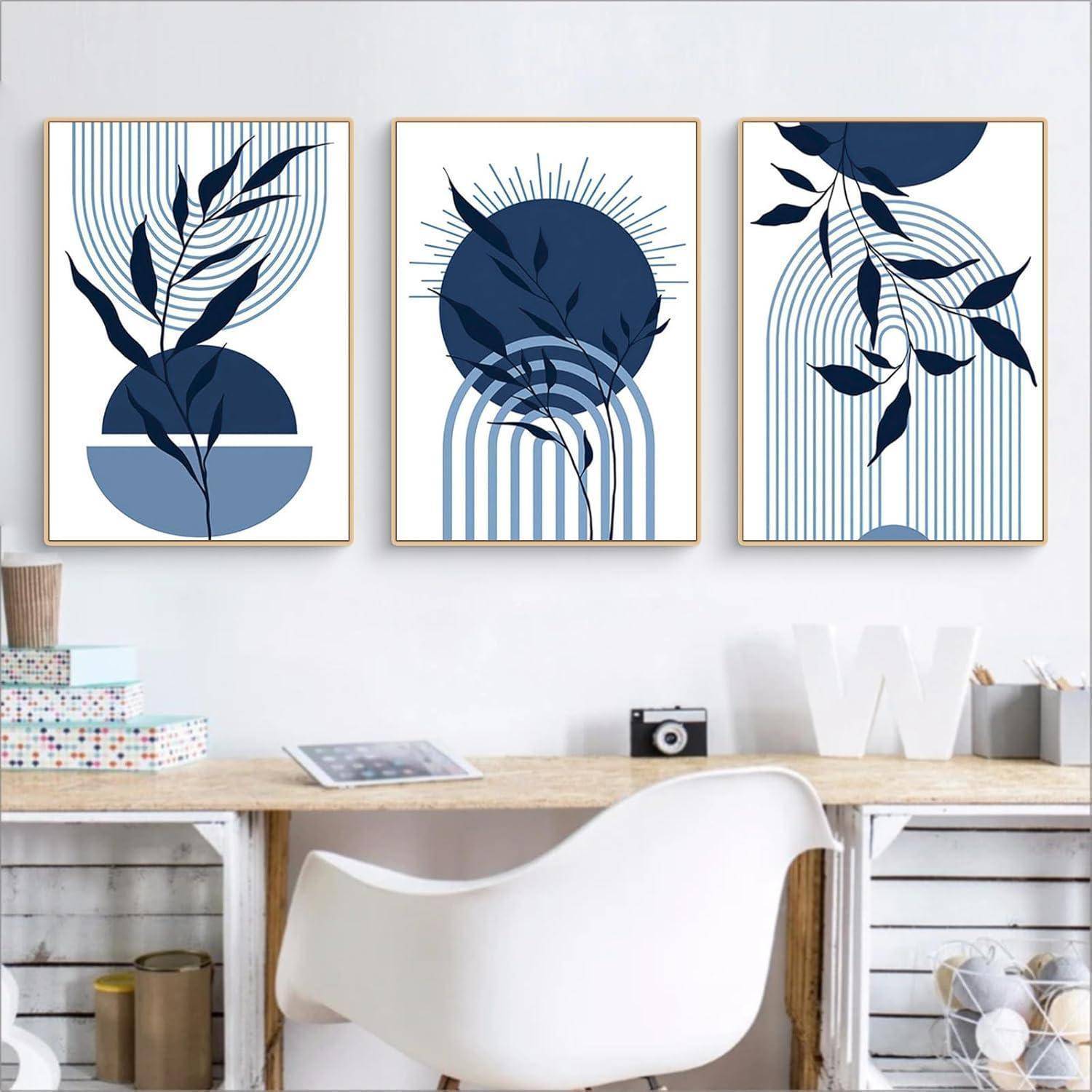 Drei gerahmte abstrakte Drucke mit blauen und weißen geometrischen und pflanzlichen Designs hängen über einem Schreibtisch mit Büchern und Dekorationsgegenständen.