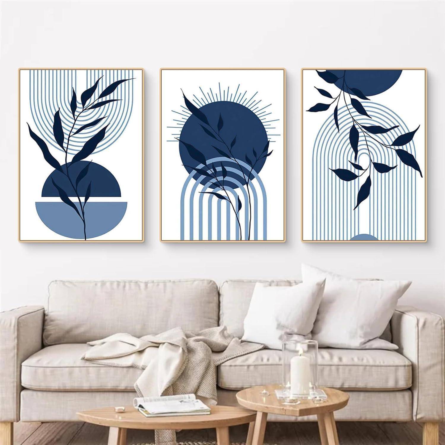 Ein minimalistisches Wohnzimmer mit einem weißen Sofa und drei abstrakten, blau-thematischen Kunstwerken an der Wand, die Blätter und geometrische Muster zeigen.