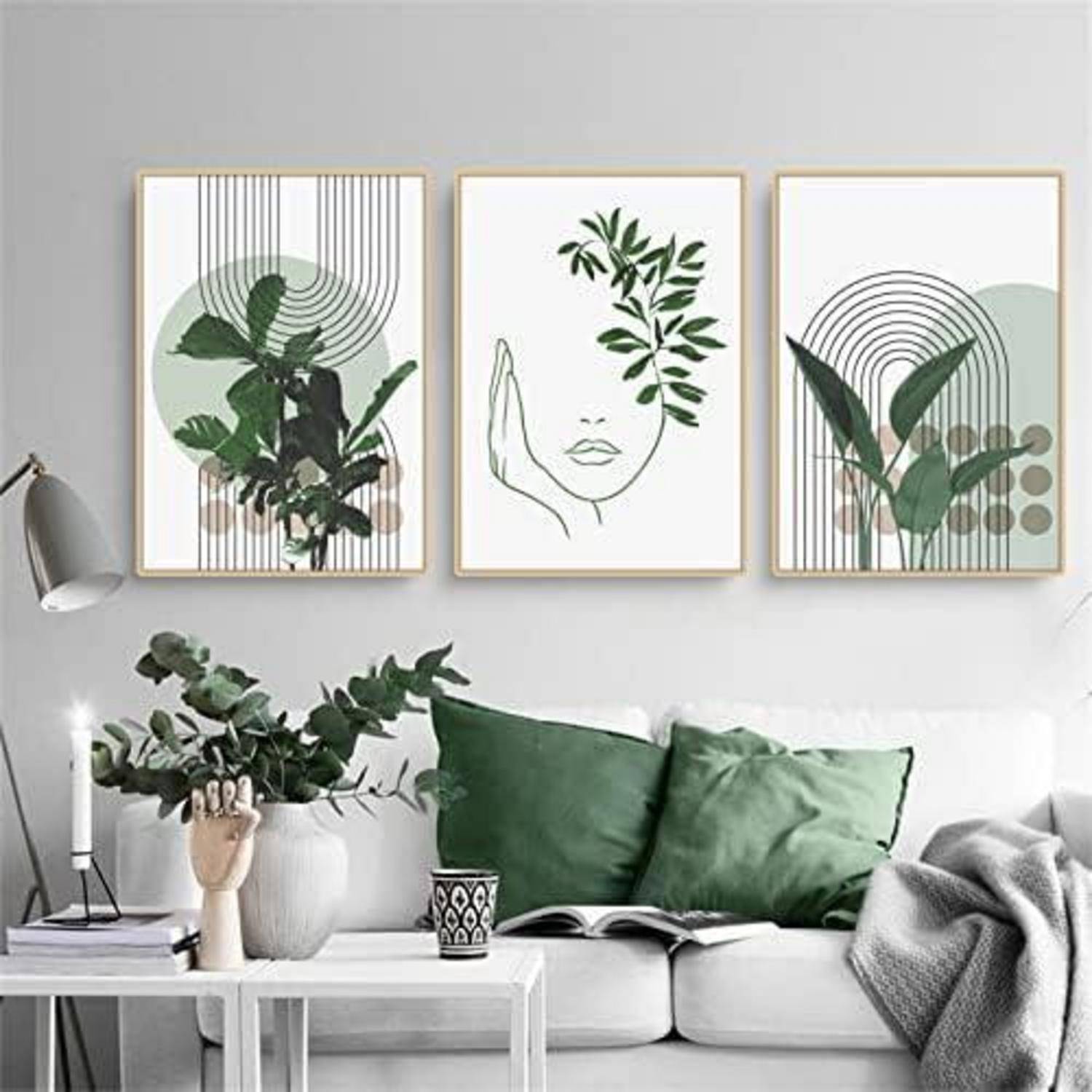 Ein Wohnzimmer mit einem weißen Sofa, grünen Kissen und einem Couchtisch; drei pflanzenthematische Kunstdrucke hängen über dem Sofa.