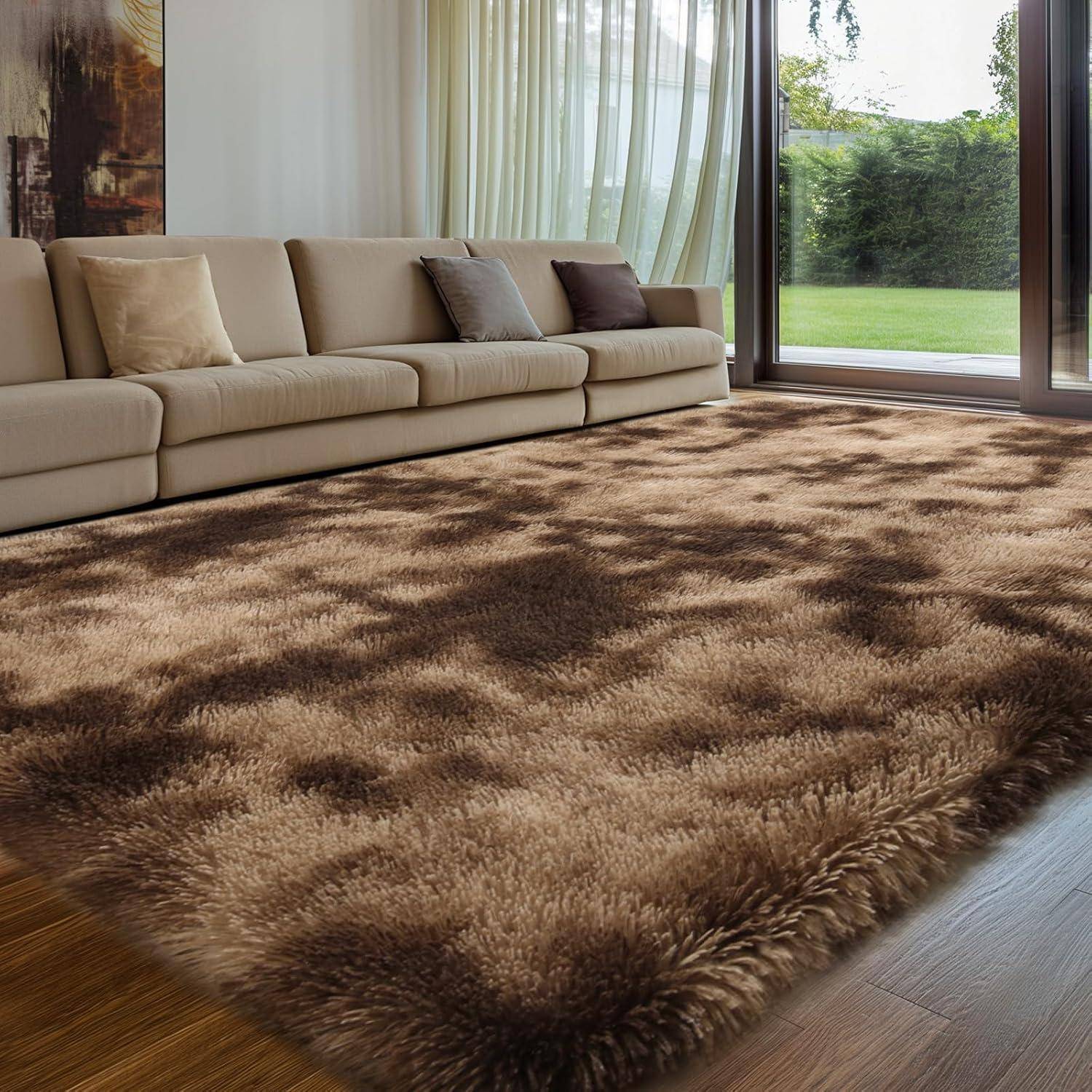 Ein Wohnzimmer mit einem langen beigen Sofa, mehreren Kissen, großen Fenstern mit transparenten Gardinen und einem flauschigen rechteckigen Teppich, der einen Holzboden bedeckt.
