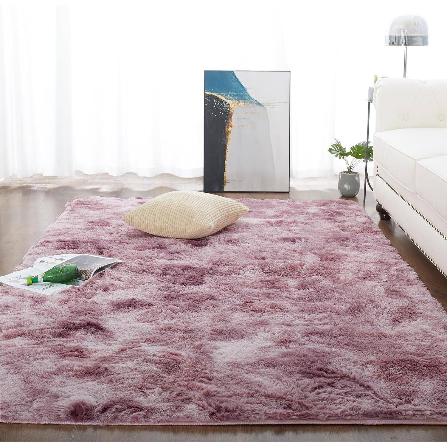 Ein flauschiger rosa Teppich bedeckt den Boden eines Wohnzimmers und zeigt ein beiges Kissen. Ein modernes Gemälde und ein weißes Sofa befinden sich im Hintergrund.