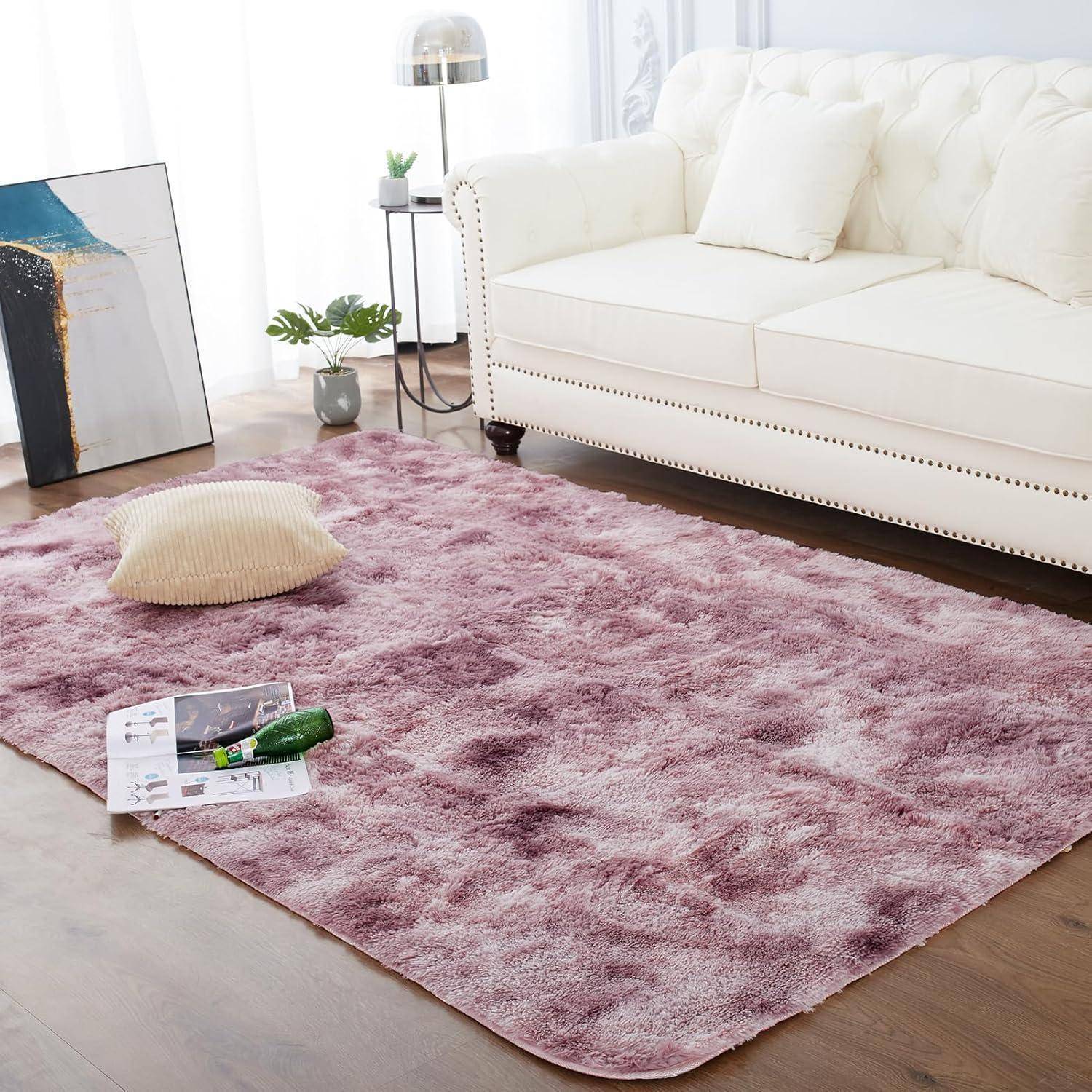 Ein Wohnzimmer mit einem weißen Sofa, einem flauschigen rosa Teppich und einem kleinen Tisch mit Dekogegenständen. Ein großes, abstraktes Gemälde lehnt an der Wand.