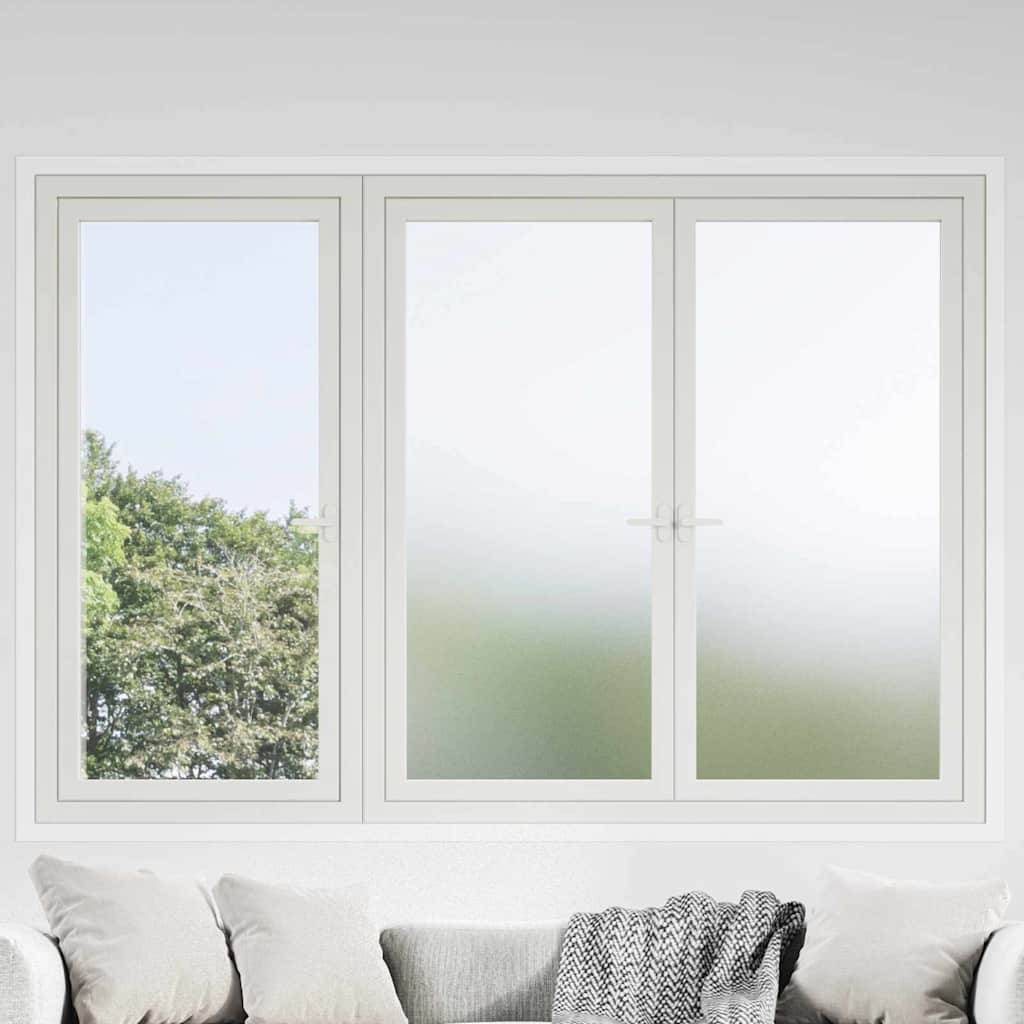 Ein großes Fenster mit zwei Scheiben, eine zeigt eine Außenansicht mit Bäumen und blauem Himmel, die andere ist mattiert für Privatsphäre, über einem Sofa mit Kissen.