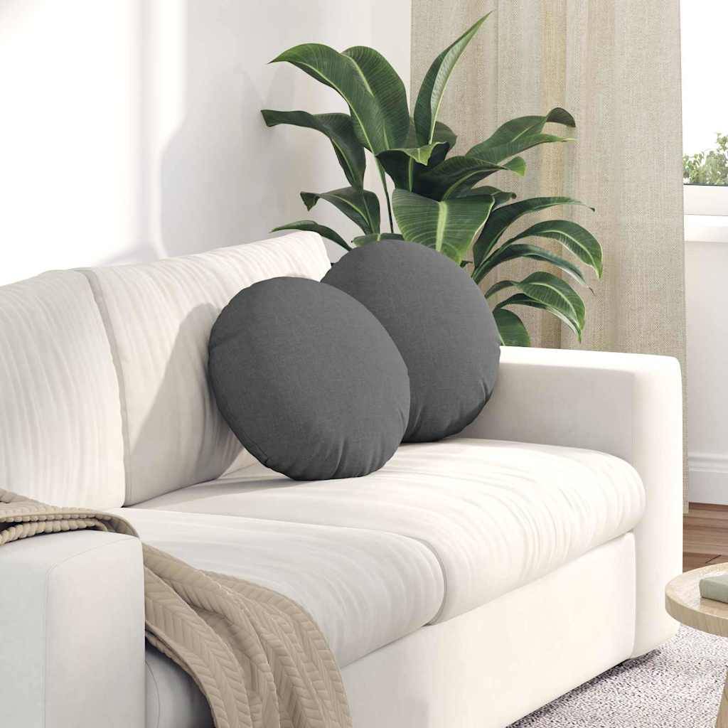 Ein weißes Sofa mit zwei runden grauen Kissen steht in einem hellen Wohnzimmer. Eine große grüne Pflanze im Hintergrund verleiht dem Raum eine natürliche Note.