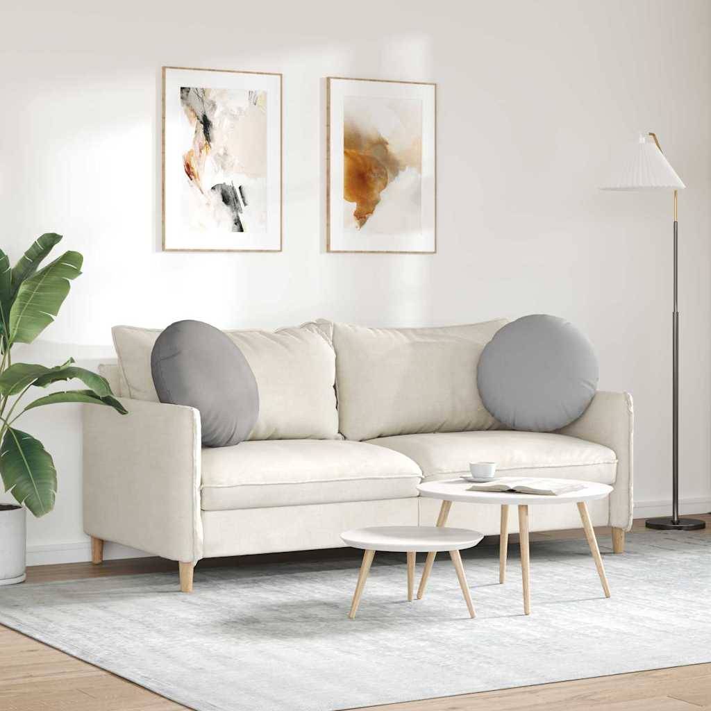 Ein modernes Wohnzimmer mit einem weißen Sofa, zwei grauen Kissen, einem kleinen Couchtisch, einer Lampe und abstrakter Kunst an der Wand.
