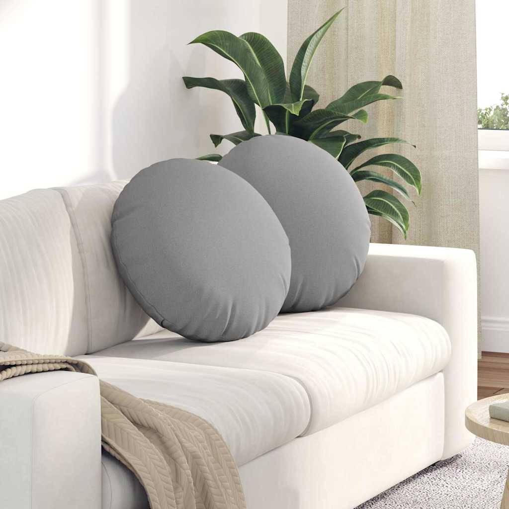 Eine weiße Couch mit runden grauen Kissen ist mit einer beigen Decke geschmückt. Eine grüne Pflanze steht in der Ecke nahe einem Fenster.
