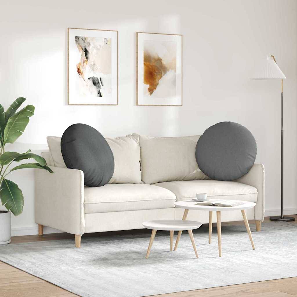 Ein modernes Wohnzimmer zeigt ein weißes Sofa mit großen grauen Kissen, einen runden Couchtisch, abstrakte Wandkunst und eine Stehlampe.