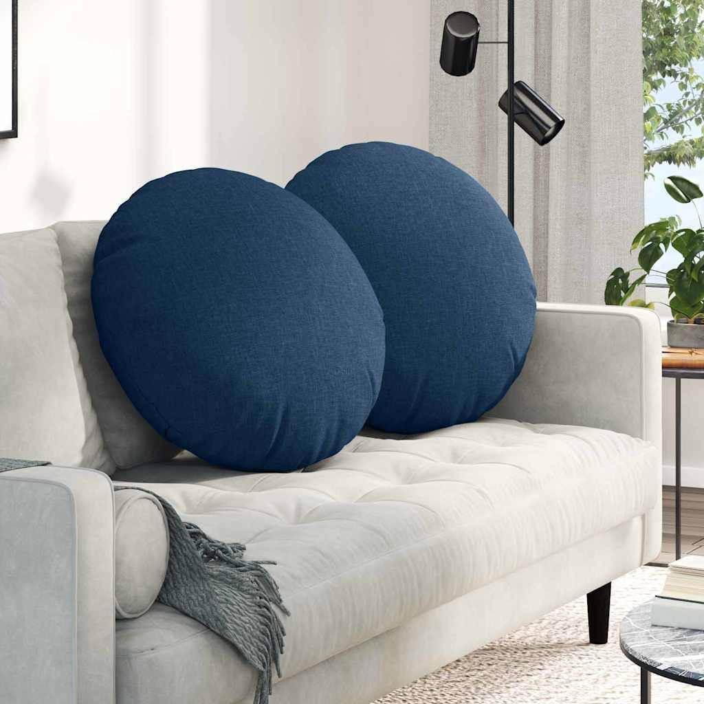 Ein gemütliches Wohnzimmer mit einem hellgrauen Sofa, auf dem zwei große, runde blaue Kissen liegen. Eine Stehlampe steht in der Nähe, während natürliches Licht hereinfällt.