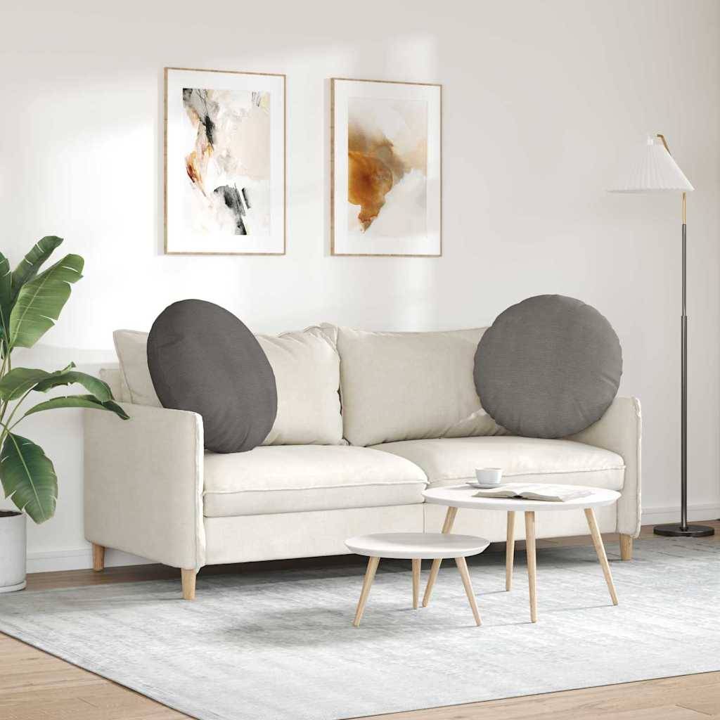 Ein modernes Wohnzimmer mit einem beigen Sofa, runden grauen Kissen, zwei abstrakten Gemälden an der Wand, einer Stehlampe und einem kleinen Couchtisch.
