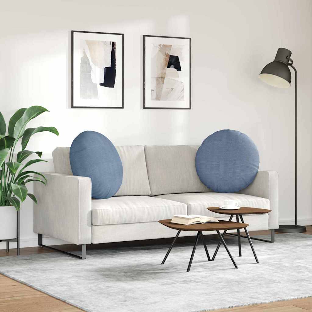 Ein modernes Wohnzimmer mit einem hellgrauen Sofa und zwei runden blauen Kissen. Zwei abstrakte Kunstwerke hängen darüber. Eine Stehlampe und eine Pflanze befinden sich in der Nähe.
