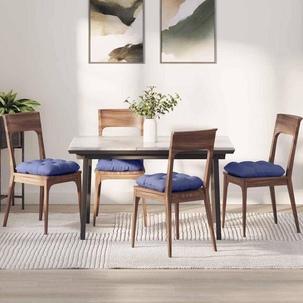 Ein Essbereich mit einem Holztisch und vier Stühlen, die mit blauen Kissen ausgestattet sind, steht auf einem gemusterten Teppich. Zwei abstrakte Kunstwerke hängen an der Wand.