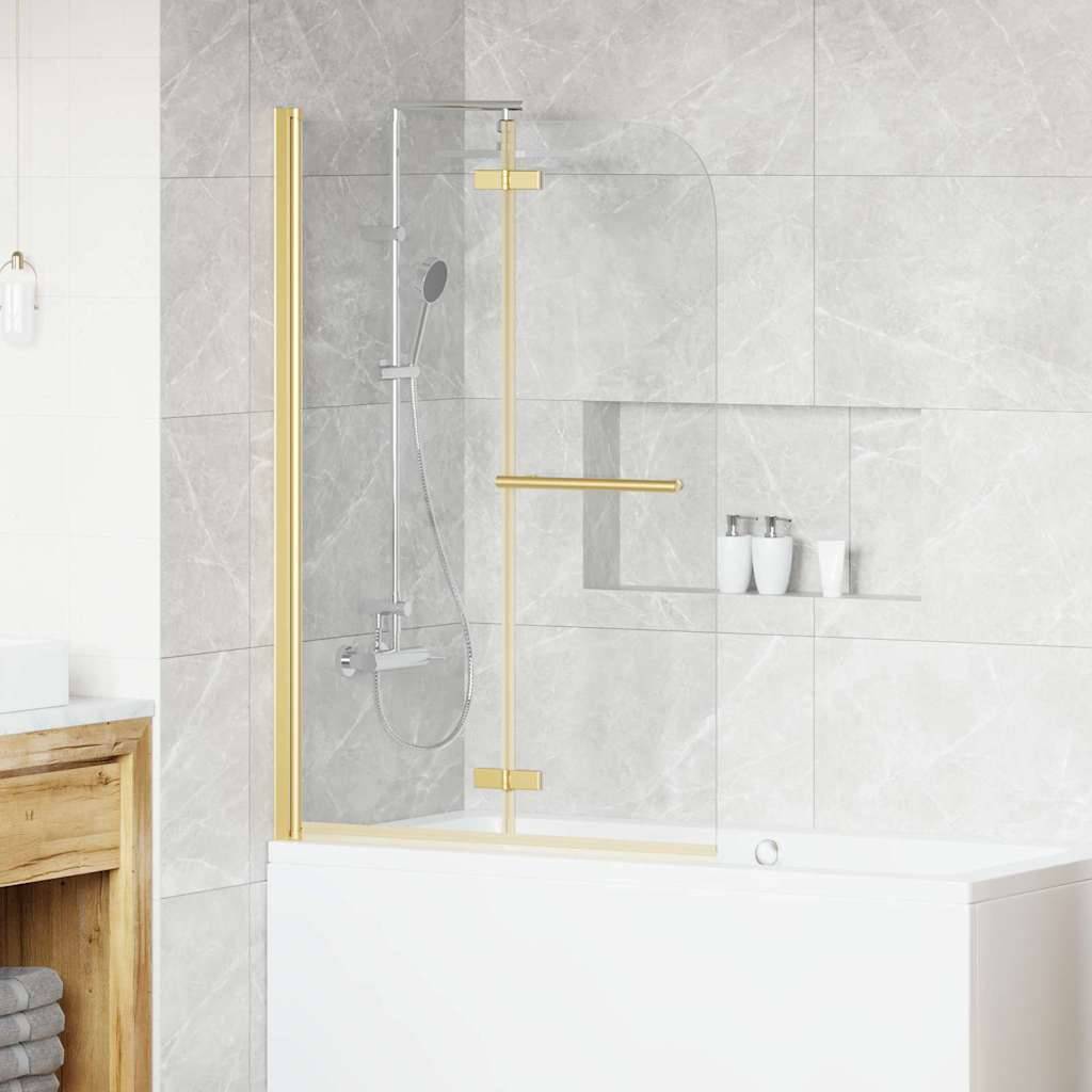 Ein modernes Badezimmer zeigt eine weiße Badewanne mit einer Glasscheibe und goldenen Armaturen. Graue geflieste Wände, Regale mit Toilettenartikeln und ein Holzschrank sind zu sehen.