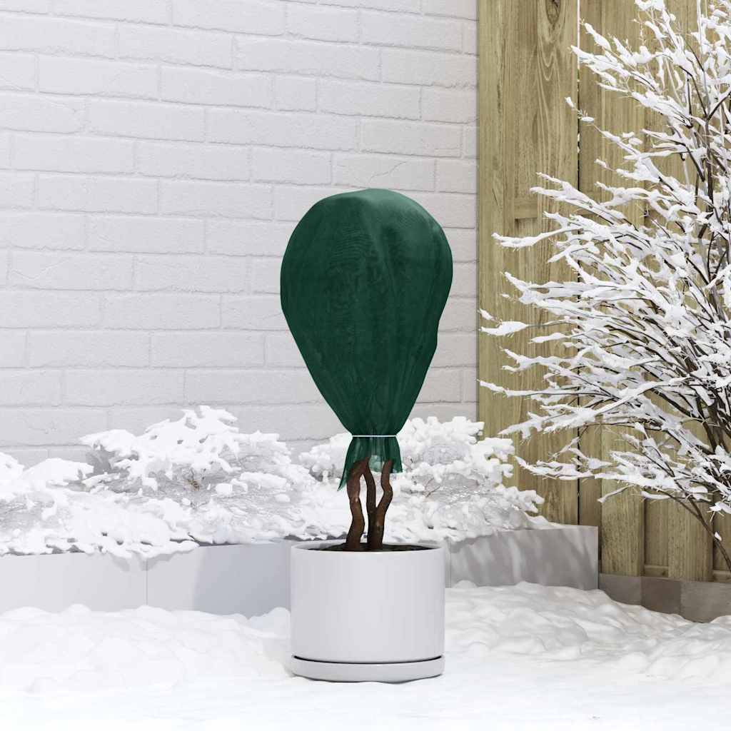 Ein Topfpflanze mit grünem Überwurf neben einem schneebedeckten Baum vor einer weißen Backsteinmauer und Holzzaun-Hintergrund.