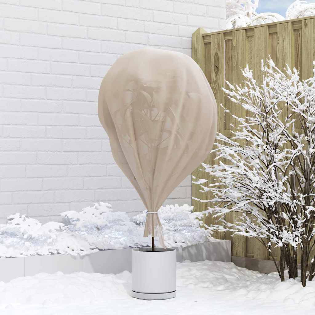 Ein Terrassenheizer, der mit einer beigen Schutzplane bedeckt ist, steht auf einer verschneiten Terrasse neben einem Holzzaun und schneebestäubten Sträuchern.