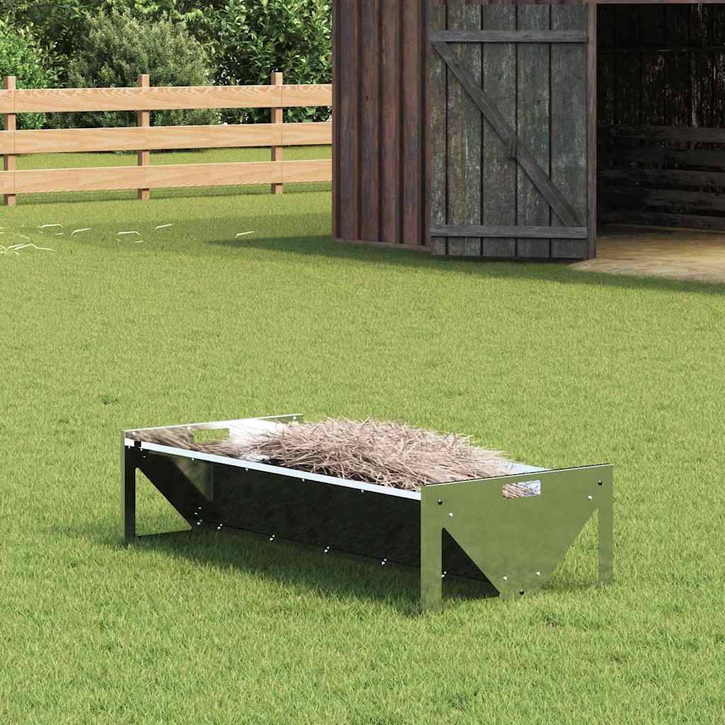 Eine Metallwanne, gefüllt mit Heu, steht auf grünem Gras in der Nähe einer Holzscheune und eines Zauns und deutet auf eine landwirtschaftliche Umgebung hin.