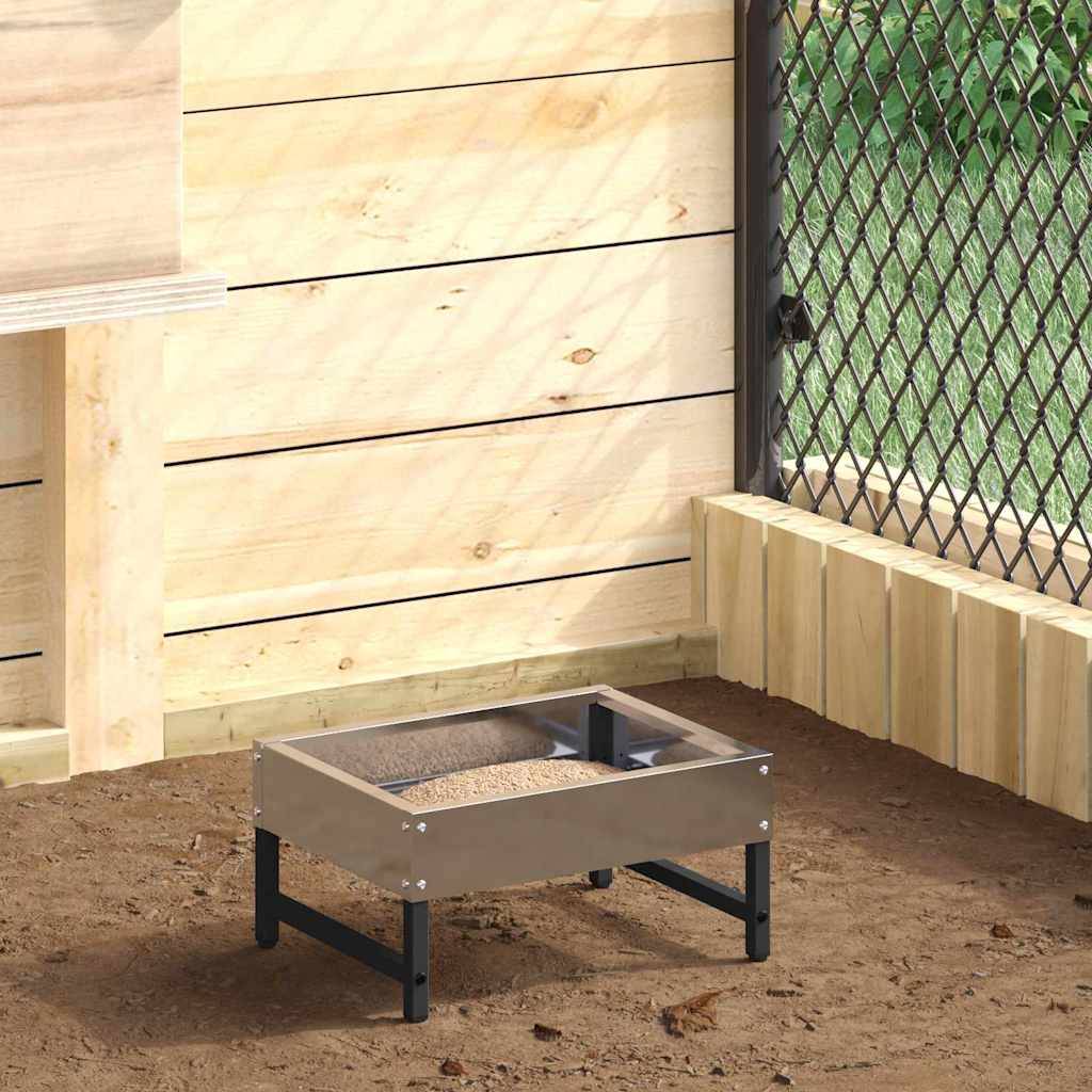 Eine geschlossene Ecke eines Hühnerstalls mit einer Holzkonstruktion, Maschendrahtzaun und einem erhöhten Metallfutterkasten auf dem Boden.