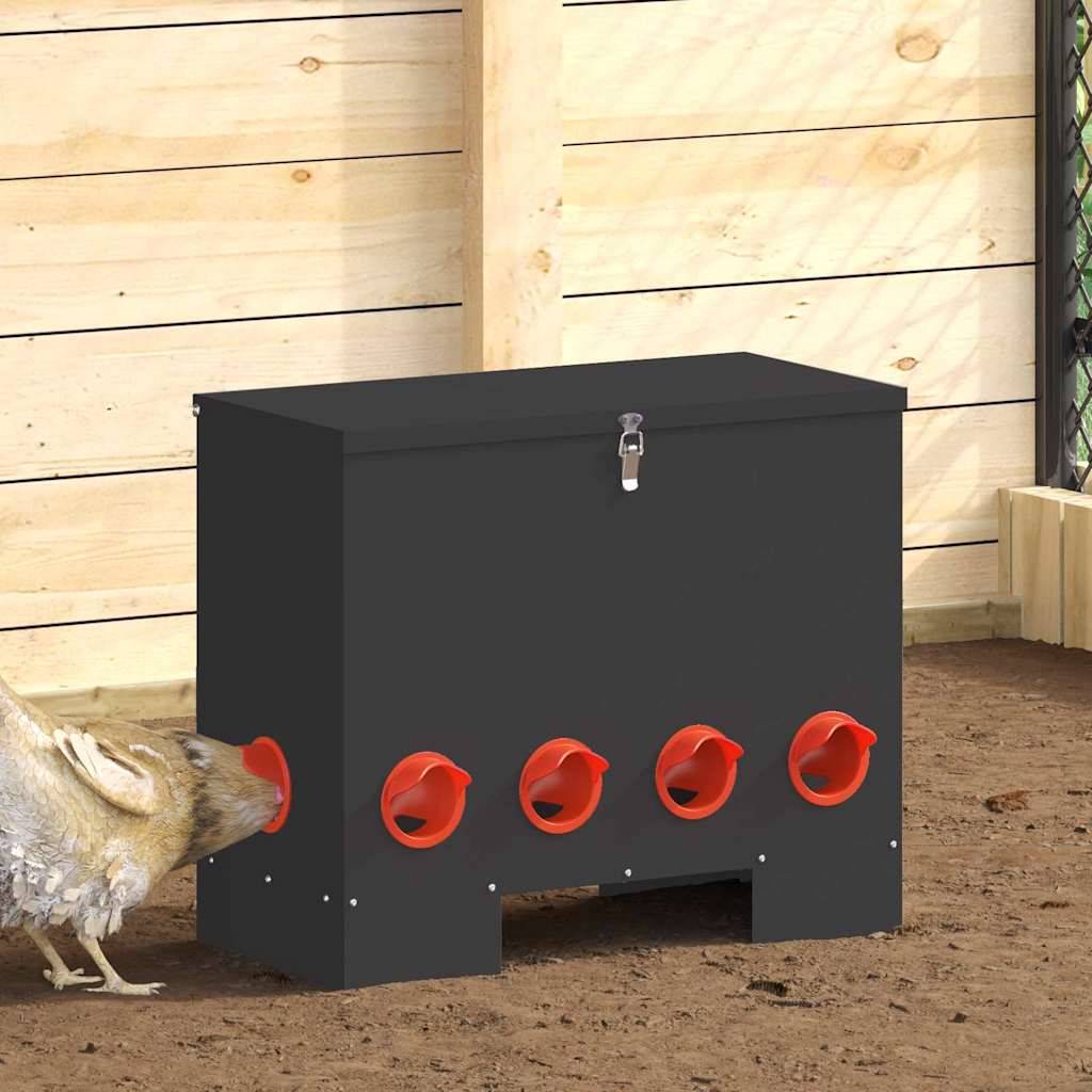 Ein Huhn pickt an einem der Löcher in einer schwarzen Futterbox mit mehreren roten Öffnungen, vor einem Holzzaun-Hintergrund.