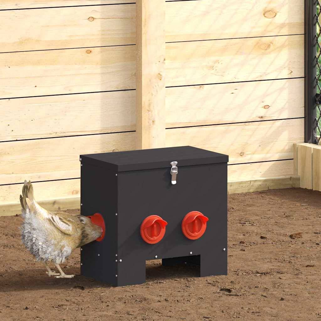 Ein Huhn frisst aus einem schwarz-roten Behälter, der an einem Holzzaun auf einem Lehmboden montiert ist und automatisierte Geflügelfütterung veranschaulicht.