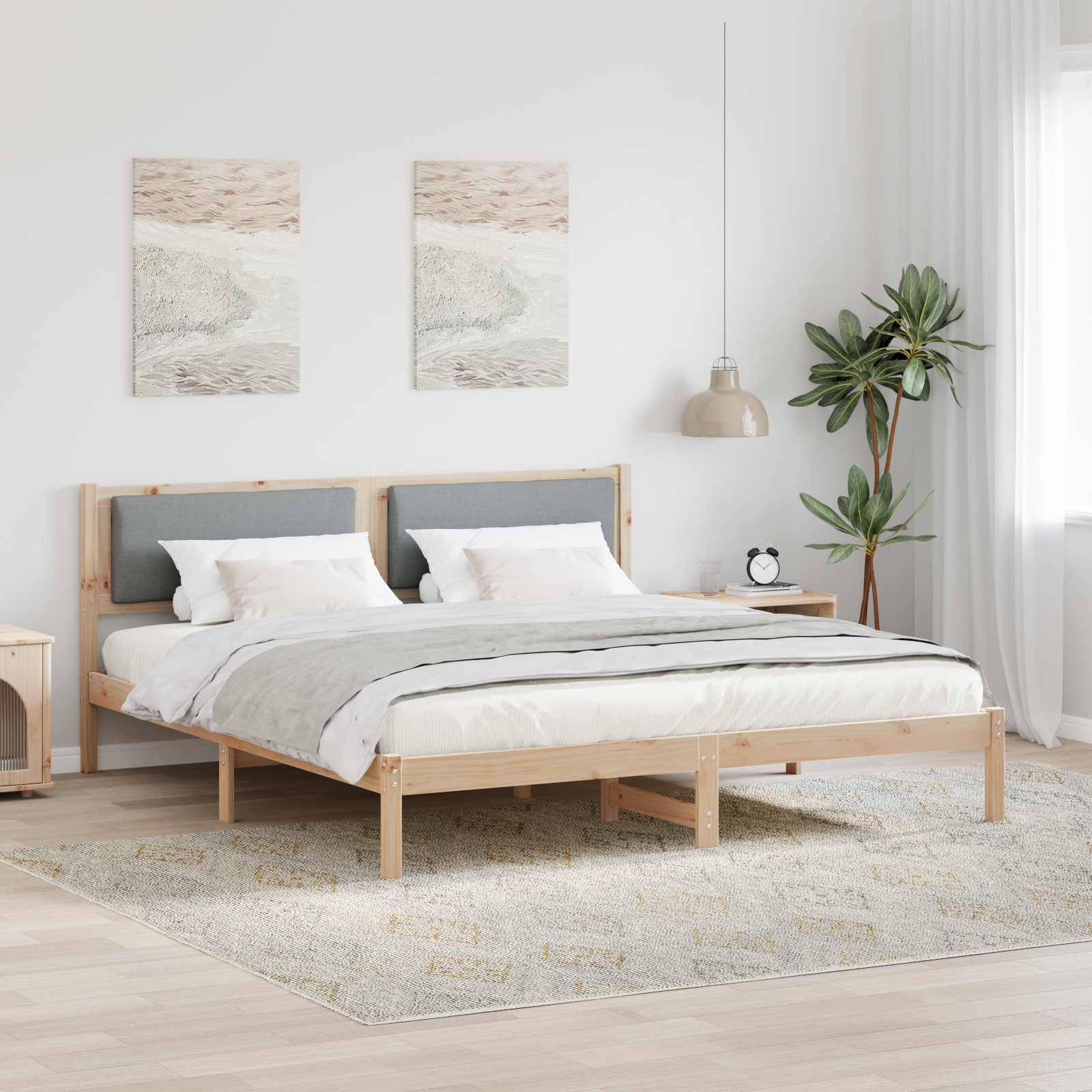 Ein minimalistisches Schlafzimmer mit einem Holzbett, weiß-grauer Bettwäsche, zwei küstengethematisierten Gemälden, einer Topfpflanze und einer Lampe auf einem Nachttisch.