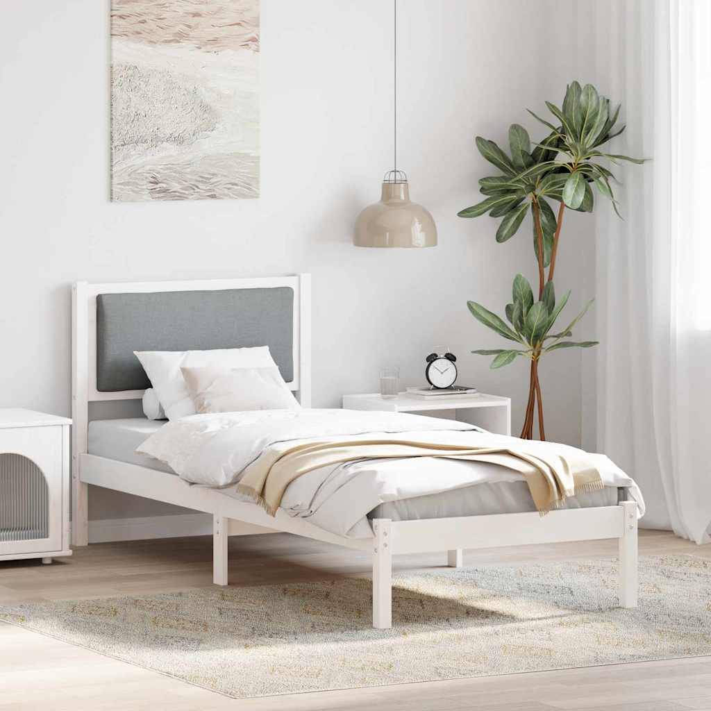 Ein minimalistisches Schlafzimmer mit einem weißen Bett, grauem Kopfteil und gemütlicher Bettwäsche. Eine große Pflanze und eine Pendelleuchte unterstreichen die ruhige Einrichtung.