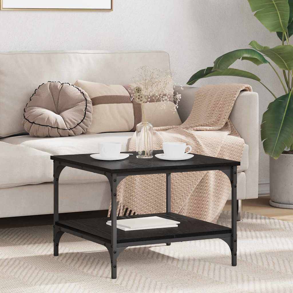 Ein gemütliches Wohnzimmer mit einem beigen Sofa, dekorativen Kissen und einer rosa Decke. Ein schwarzer Couchtisch mit Büchern und Vasen steht auf einem gemusterten Teppich.