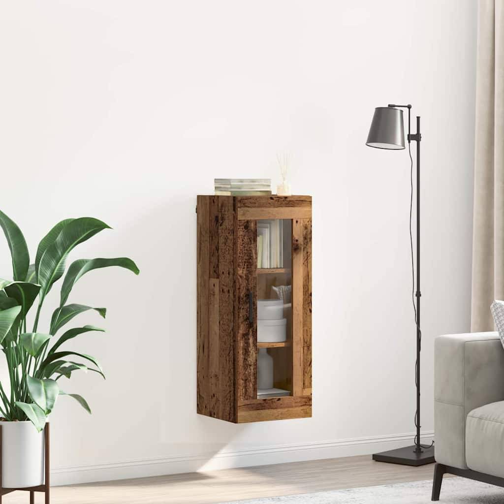 Ein kleiner Holzwandschrank mit Glastür ist an einer weißen Wand montiert und enthält dekorative Objekte. Eine Stehlampe steht daneben.