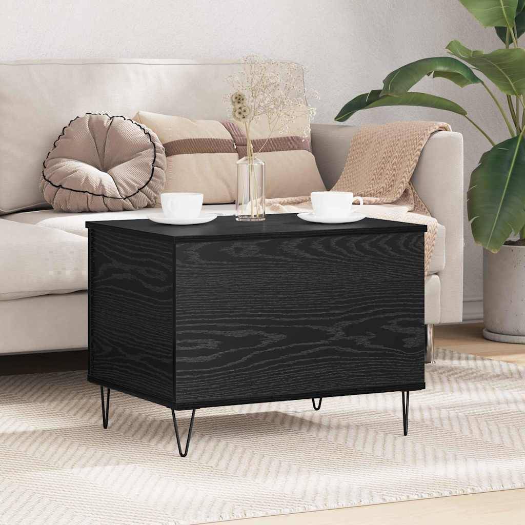 Ein schwarzer Holz-Couchtisch mit Hairpin-Beinen, auf dem zwei Teetassen und eine Vase mit getrockneten Blumen stehen, befindet sich vor einem beigen Sofa.