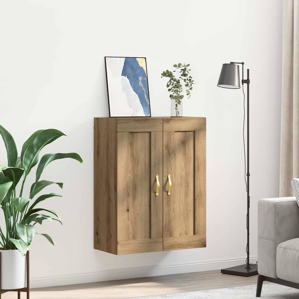 Ein Wandschrank aus Holz mit zwei Türen, Messinggriffen und einem minimalistischen Kunstwerk sowie einer kleinen Pflanze obenauf. Er steht neben einem grauen Sofa und einer hohen Stehlampe.