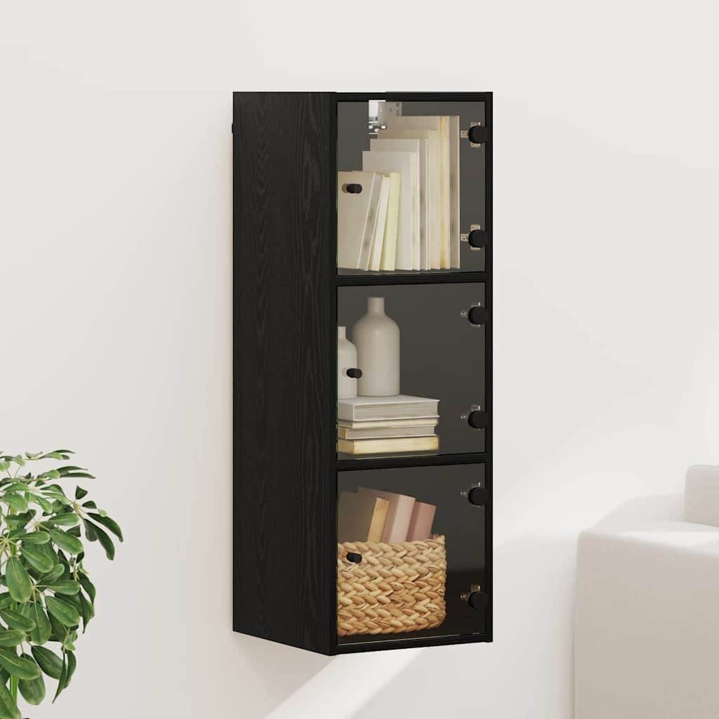 Ein an der Wand befestigtes schwarzes Regal mit drei Glasfront-Regalen. Die Regale sind mit Büchern, Dekoartikeln und einem Flechtkorb bestückt. Eine Pflanze steht in der Nähe.