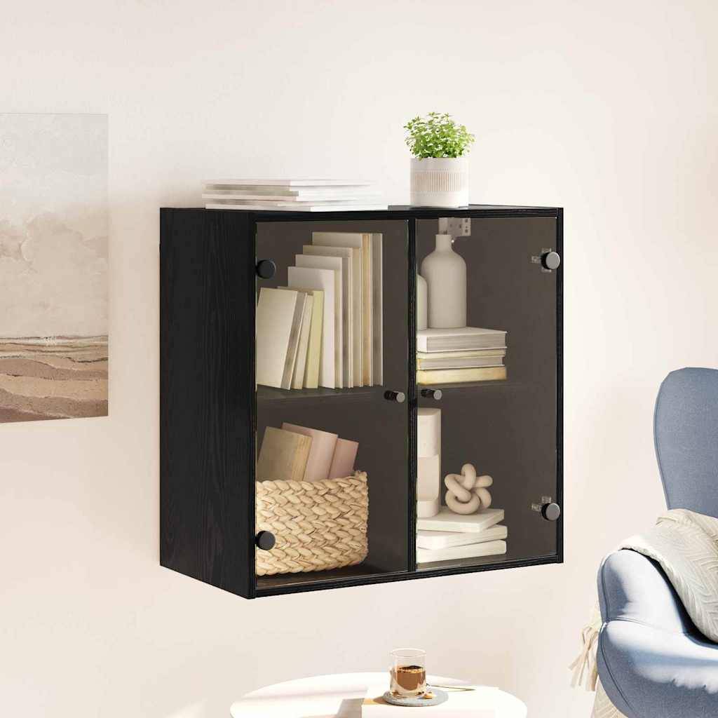 Schwarzer, an der Wand montierter Schrank mit Glastüren, in dem Bücher, ein Flechtkorb, Dekorationsgegenstände untergebracht sind und auf dem eine kleine Pflanze steht.