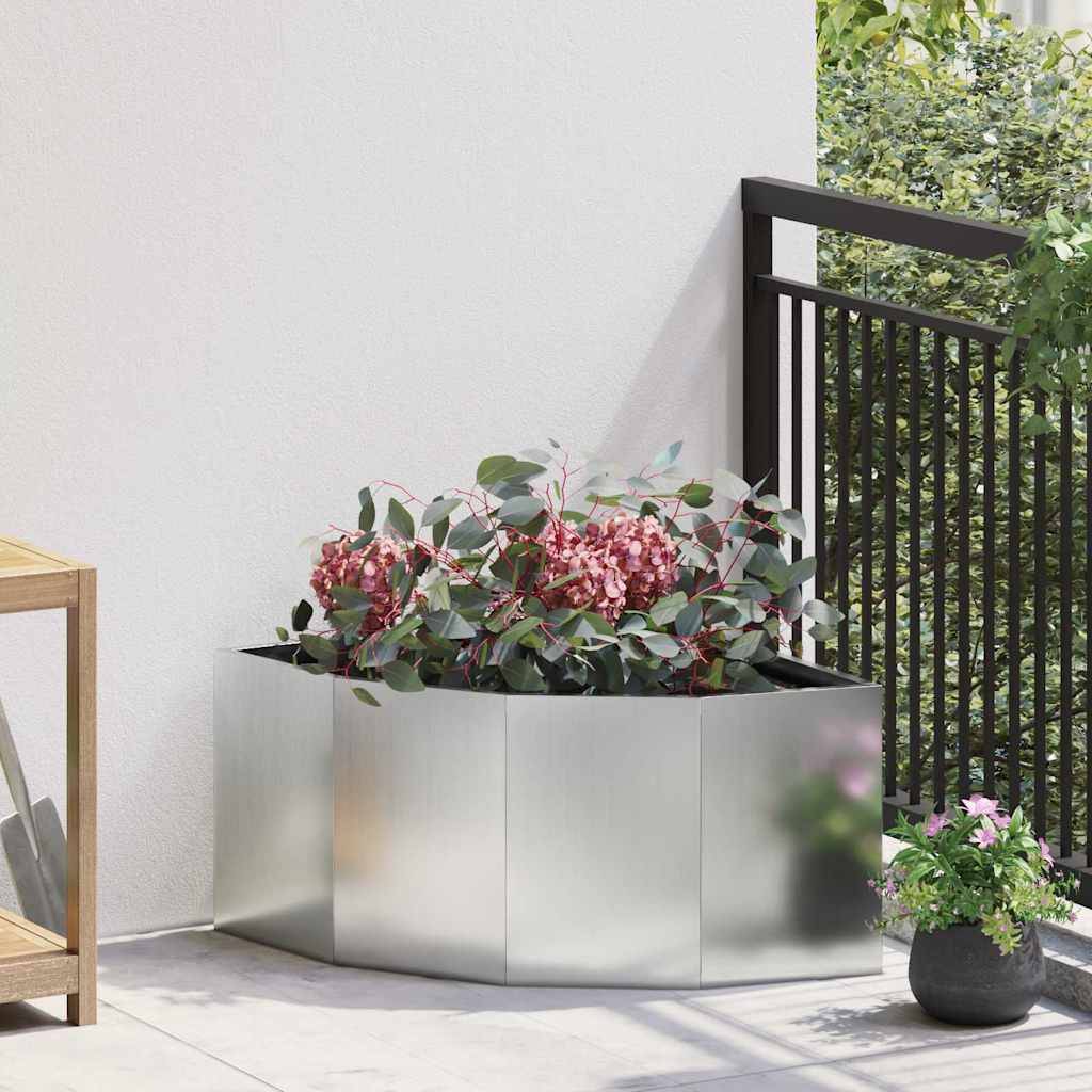 Rechteckiger Pflanzkübel mit roten Blumen auf einer sonnenbeschienenen Terrasse, neben einem schwarzen Metallgeländer und einem Holzstuhl.