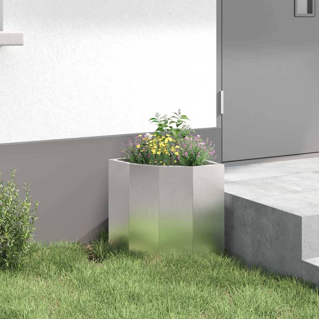 Ein Betonpflanzer mit gelben und lila Blumen steht nahe dem Hauseingang, umgeben von grünem Gras und einem kleinen Strauch.