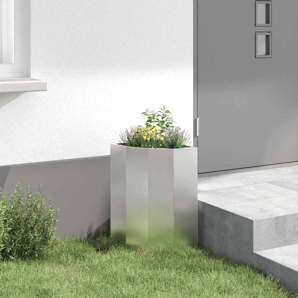 Eine moderne Außenszene zeigt eine Ecke eines minimalistischen Hauses mit einem kleinen Garten. Ein schlanker, hoher Pflanzkübel trägt grüne Sträucher an einer grauen Wand.