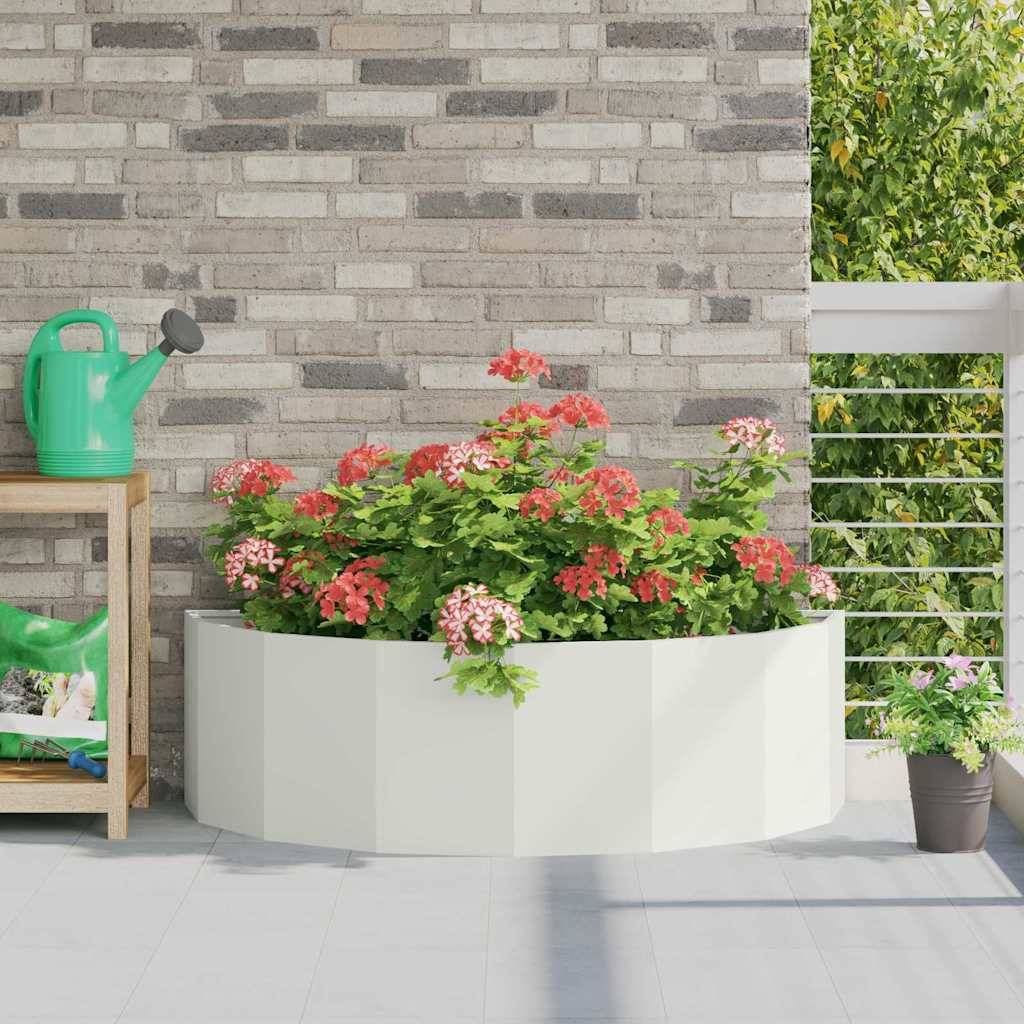 Rechteckiges Pflanzgefäß mit lebhaften rosa und grünen Blumen auf einer Terrasse vor einer Backsteinmauer; eine Gießkanne und eine Bank in der Nähe.