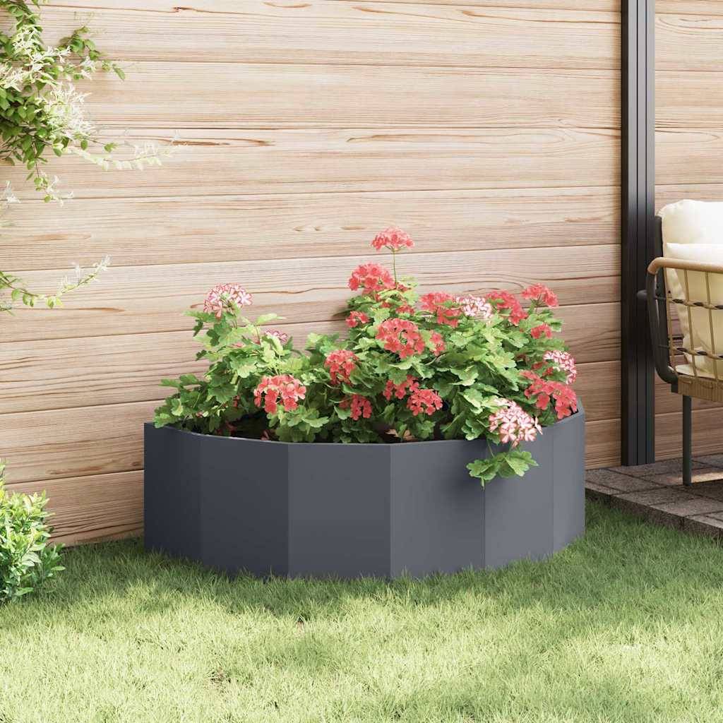 Ein moderner sechseckiger Pflanzkübel mit blühenden roten und rosa Blumen steht auf einem üppigen grünen Rasen, begrenzt von einem Holzzaun.