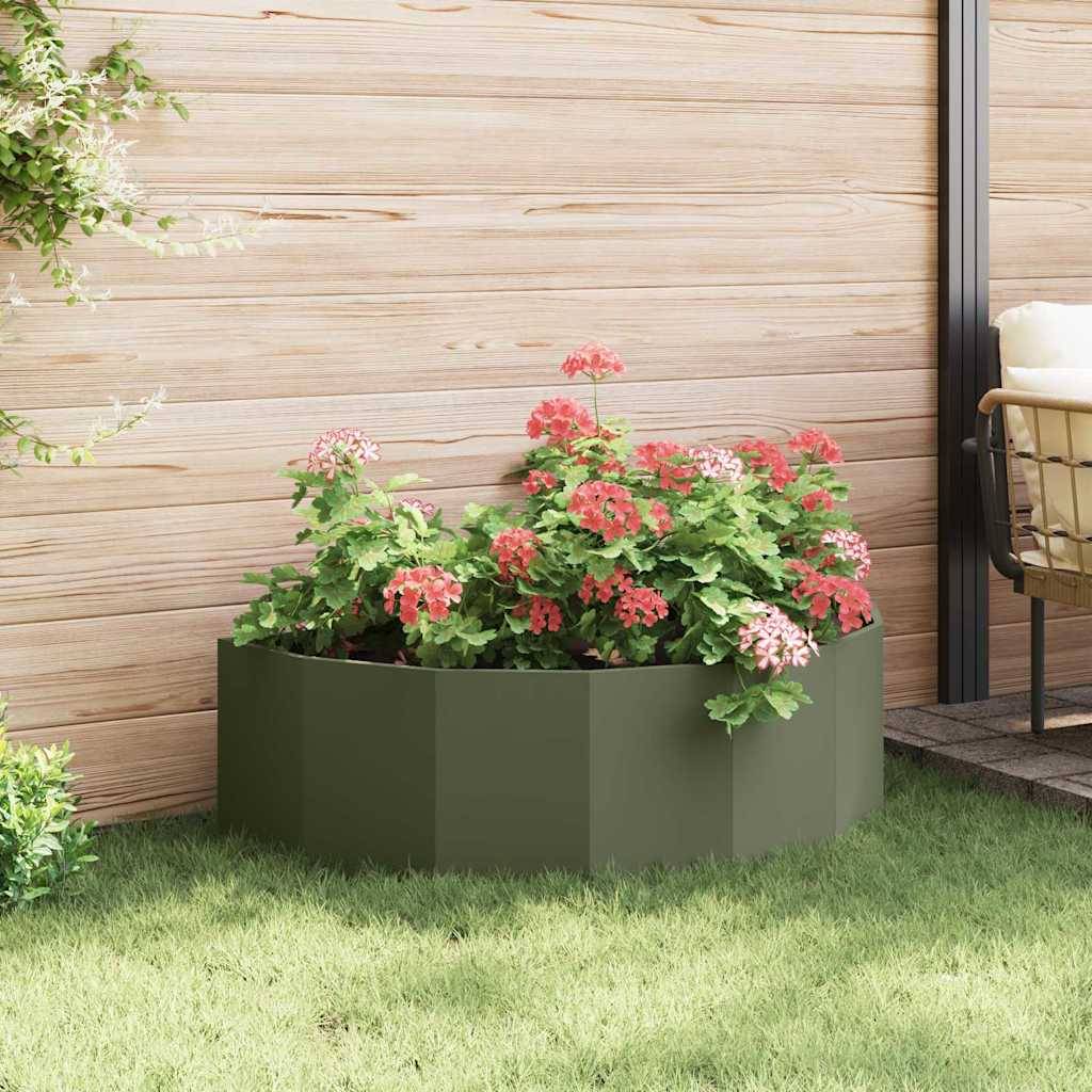 Ein Blumenbeet mit leuchtend roten und rosa Blüten ist vor einem Holzzaun auf einer Rasenfläche angelegt, in dessen Nähe ein Holzstuhl steht.