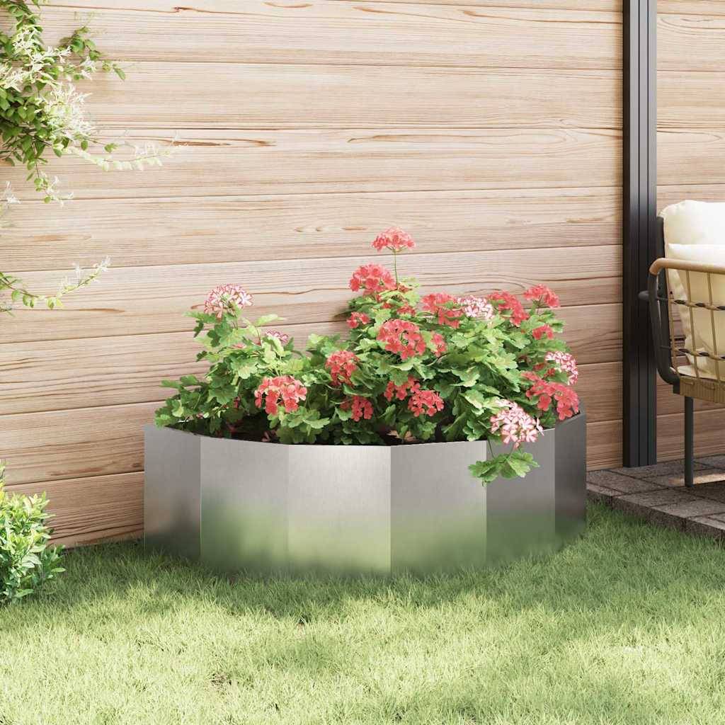 Metallblumenkasten mit leuchtend roten und rosa Blumen auf Gras. Holzzaun im Hintergrund, der eine beschauliche Gartenszene schafft.