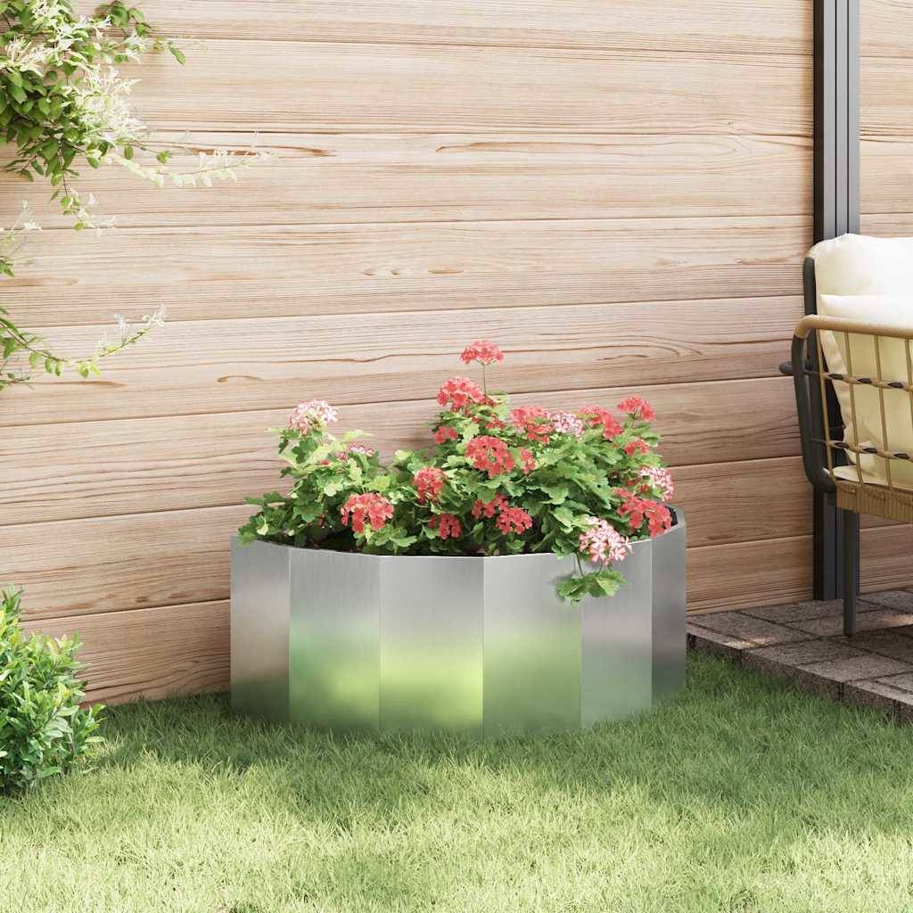 Eine Holzterrasse mit einem Metallpflanzer, der blühende rote und rosa Blumen enthält. Ein Holzstuhl ist am Rand der Terrasse teilweise zu sehen.