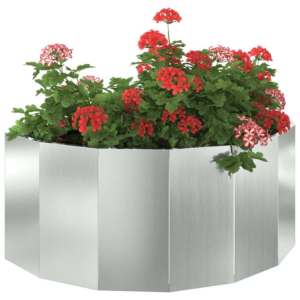 Ein silberner sechseckiger Pflanzkasten mit lebhaft roten und rosa Blumen, umgeben von grünem Blattwerk, vor einem schlichten Hintergrund.