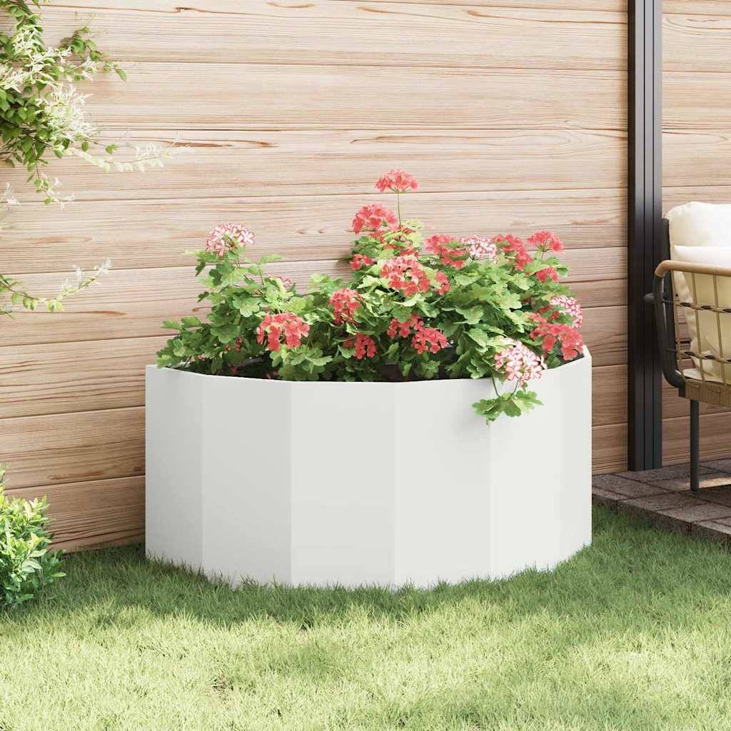 Ein weißer sechseckiger Pflanzkübel, gefüllt mit blühenden rosa und roten Blumen, steht auf einer Holzterrasse, mit etwas Grünzeug im Hintergrund.